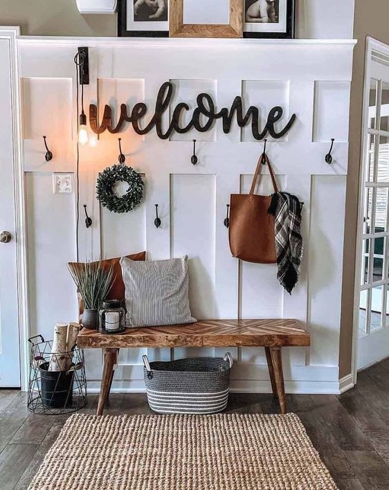 a cozy farmhouse entry with a jute rug, a wooden bench, a sign, bulbs and a wreath plus some candle lanterns