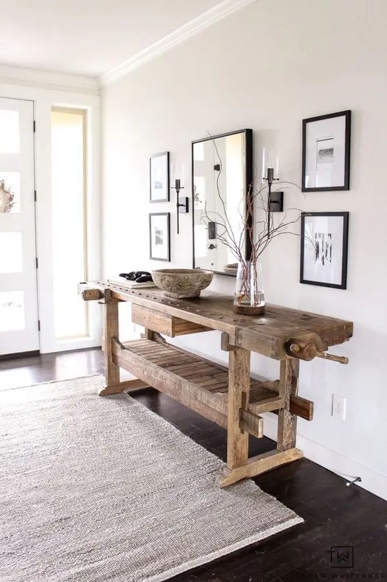 a delicate and airy greige entryway with a mini gallery wall with black frames, a stained vintage table, a neutral rug and lots of natural light