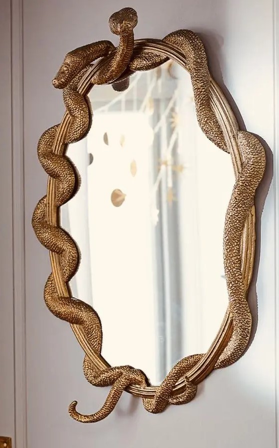 a mirror in a gilded frame with gold snakes is a chic and refined decor idea for Halloween