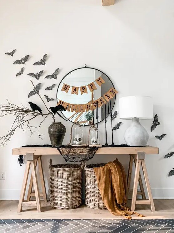 a cool Halloween console table styled with black cheesecloth, baskets and blankets, a vase with branches, bats and blackbirds, a couple of banners