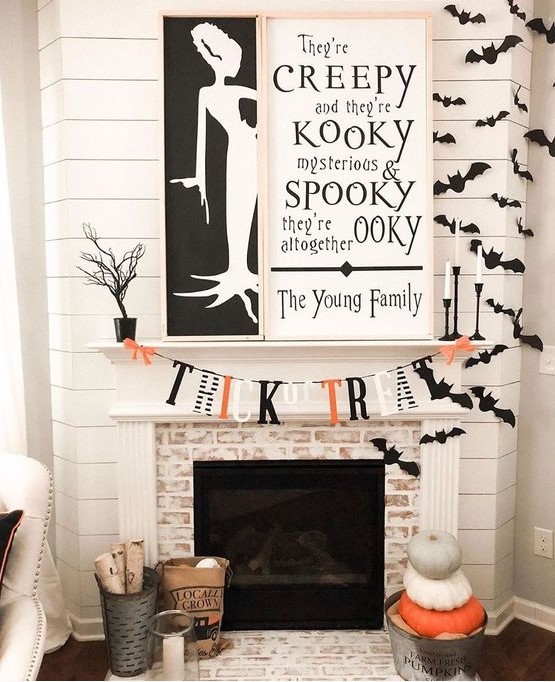an elegant contrasting fireplace with two monochromatic signs, bats, a bright bunting and stacked pumpkins