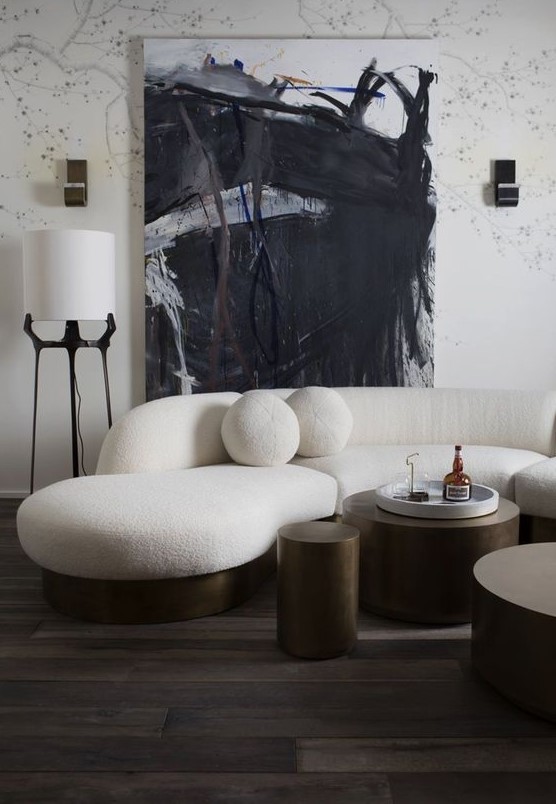 a monochromatic living room with a creamy curved sofa and round pillows and dark metal round tables