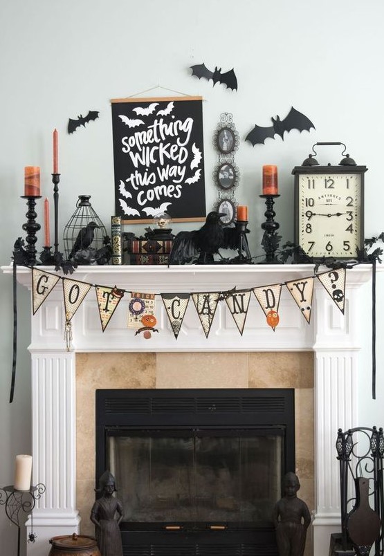 a vintage Halloween mantel with a bunting, blackbirds, orange candles, bars and vintage books and clocks