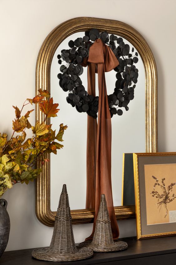 elegant Halloween mirror decor with a black foliage wreath and a rust ribbon bow is amazing