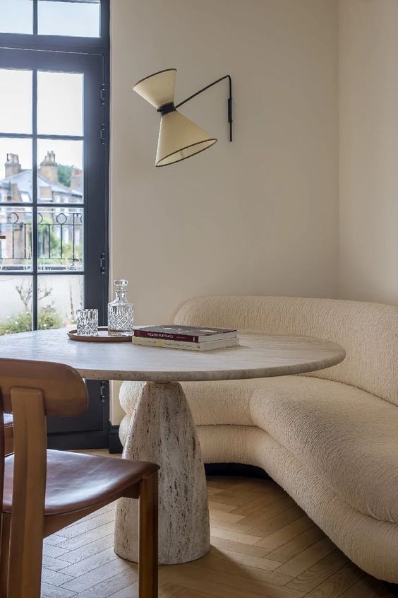 a neutral curved sofa, a stone table, a leather chair and a sconce are a cool combo for a dining nook