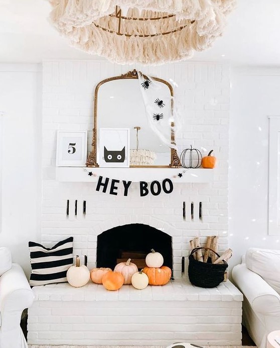 a chic Halloween mantel with spiderweb and spiders on the mirror, pumpkins, a black garland and pumpkins in the fireplace