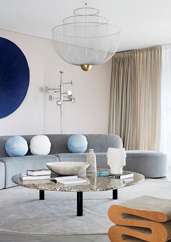 a neutral living room made bold with a curved grey sofa, a navy artwork and a marble coffee table and a cork stool
