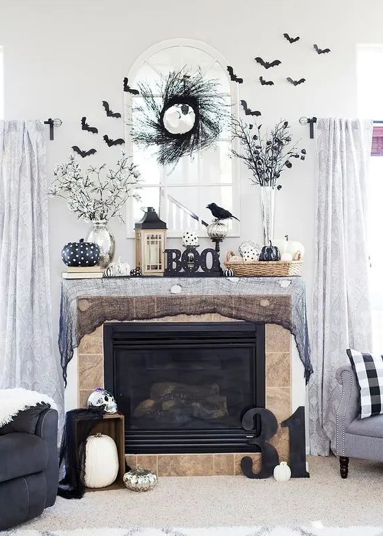 a black Halloween mantel with black cheesecloth, bats, branches, black and white pumpkins, lanterns and blackbirds