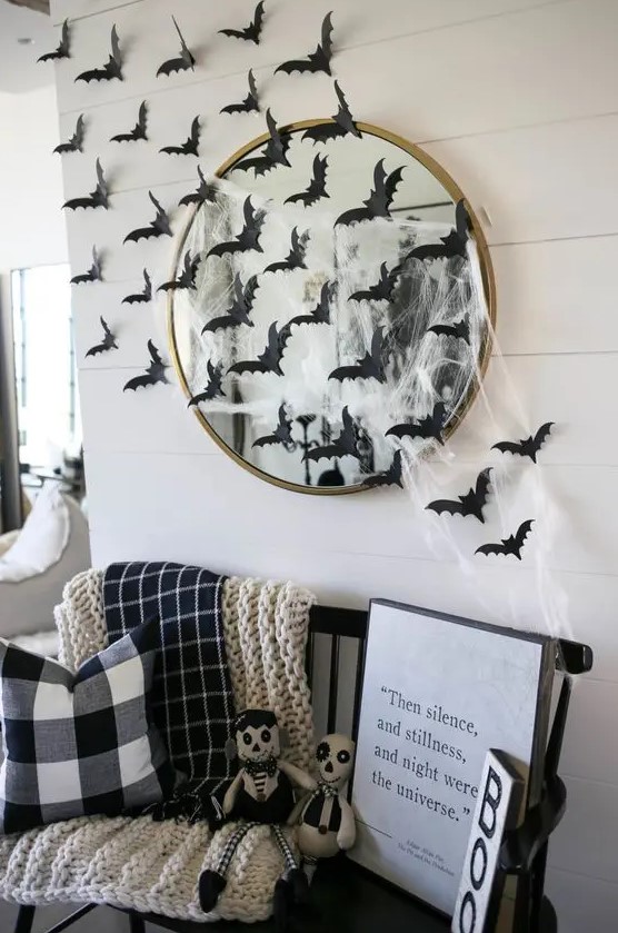 a black bench styled with blankets and pillows, with signs and scary toys plus a hautned mirror with spiderweb and black paper bats