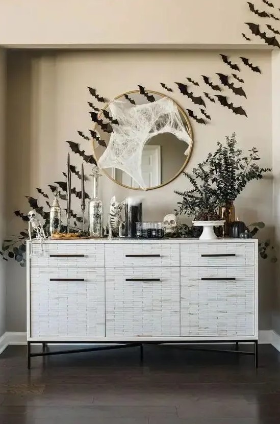 a cool console table with black bats, greenery in vases, skulls and skeletons, spiderwebs is a gorgeous idea for Halloween