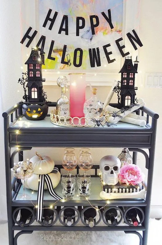 a glam Halloween bar cart with scary houses, skulls, a pink bloom, neutral pumpkins, lights and a black letter banner