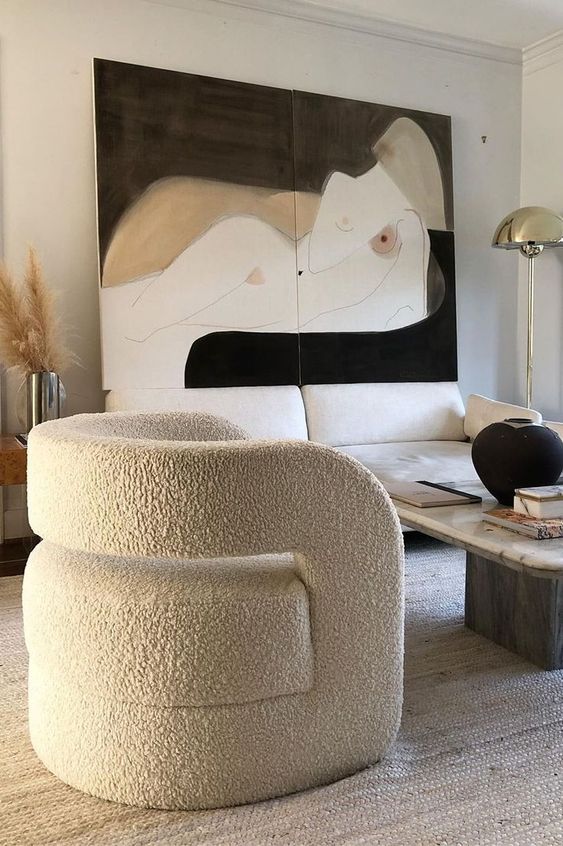 a refined living room with a creamy sofa, a coffee table, a curved chair, a statement artwork and pampas grass