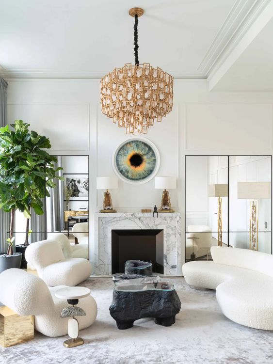 a sophisticated living room with a marble clad fireplace, a curved creamy sofa and matching chairs, black coffee tables, a quirky chandelier
