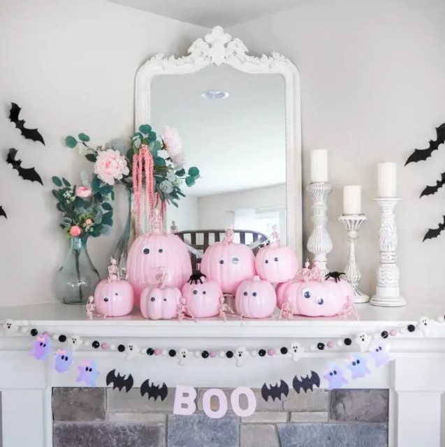 a Halloween mantel with pink pumpkins with googly eyes, banners with ghosts and bats, blooms and candles in white candleholders