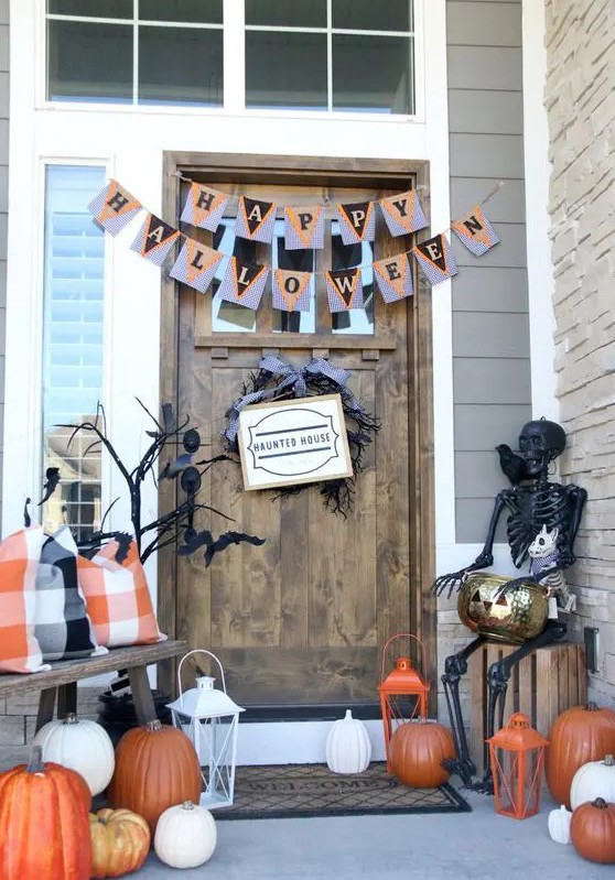 a Halloween porch with white and orange pumpkins, candle lanterns, buntings, a black skeleton and black branches plus a twig wreath