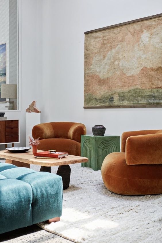 a colorful living room with rust-colored curved chairs, a green coffee table, a coffee table, a blue ottoman, an artwork and a sideboard