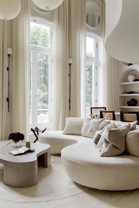 a sophisticated modern living room with a neutral curved sofa, a curved coffee table, a modern dining space with cane chairs