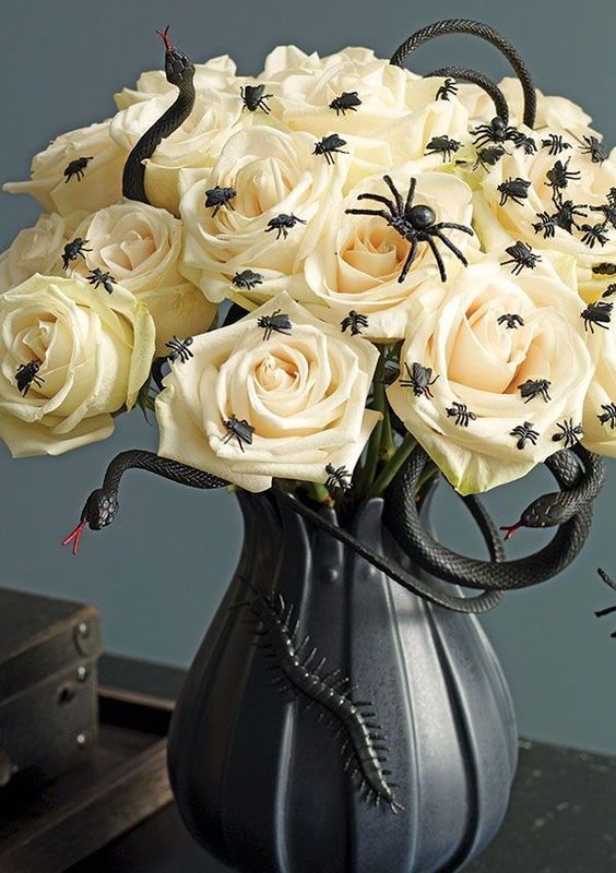a Halloween centerpiece of a black vase with white roses, black snakes, spoders and flies is a catchy and bold idea