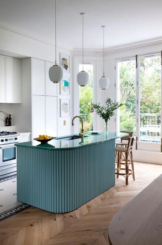 a beautiful modern kitchen with white cabinets, a blue fluted and curved kitchen island, pendant lamps and an eating zone