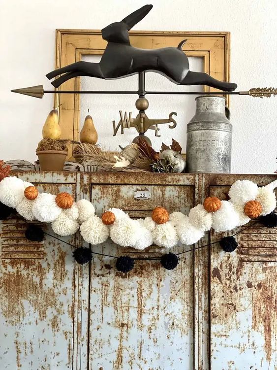 a black pompom and white pompom Halloween garland with little orange pumpkins is great not only for Halloween but also for the fall