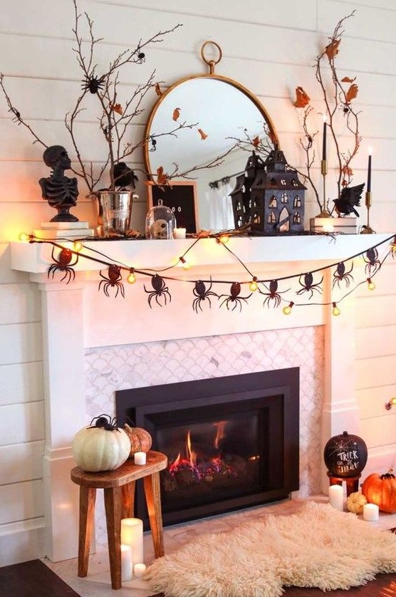 a catchy Halloween mantel with a spider garland, lights, branches with leaves, a scary house and some pumpkins on the floor