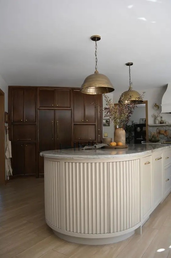 a dark-stained kitchen with a light-colored fluted curved kitchen island that contrasts the cabinetry and stainds out in its backdrop