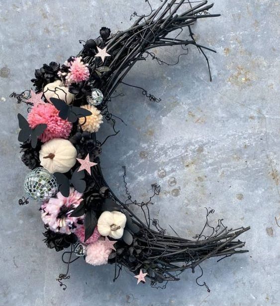 a creative moon-shaped Halloween wreath with pink pompoms, little pumpkins, black butterflies, a disco ball and some stars