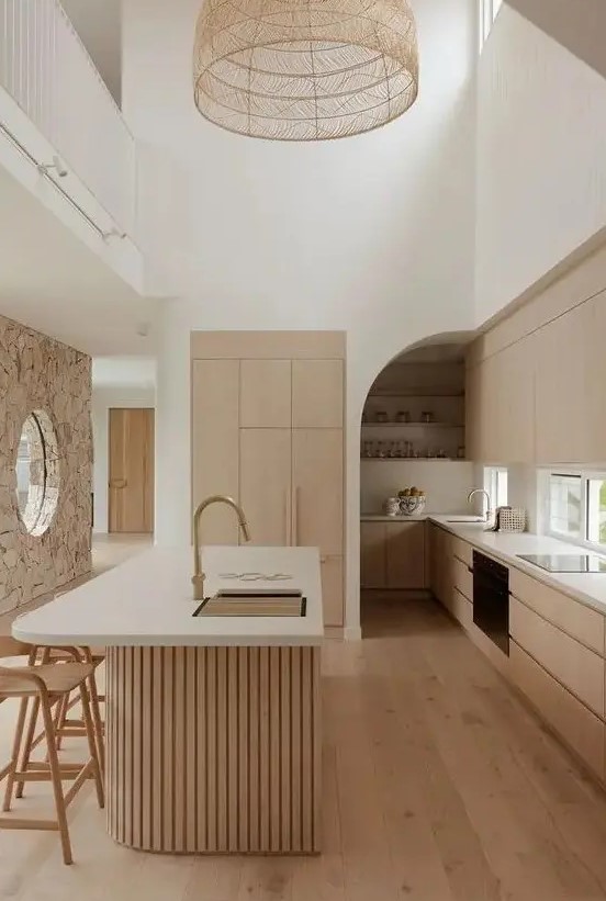 a light-stained minimalist kitchen with sleek cabinets, a window backsplash, a curved fluted kitchen island with a curved part and a woven pendant lamp