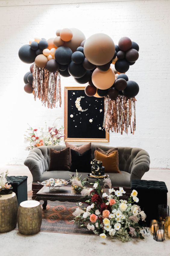 a gorgeous celestial Halloween lounge with dark seating furniture, a balloon installation, a moon wall art and some blooms