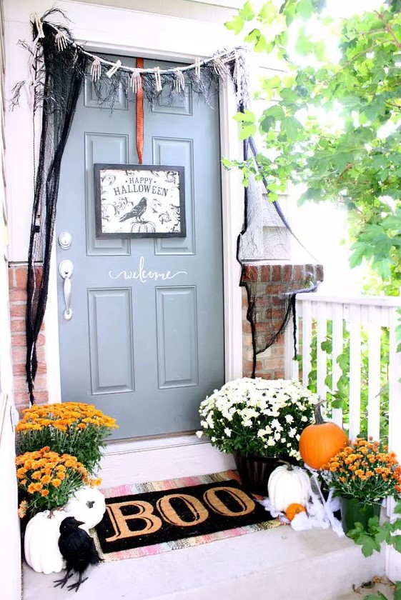 a Halloween front door with a black sign, skeleton hands and black spiderweb, a black mat and a blackbird plus pumpkins