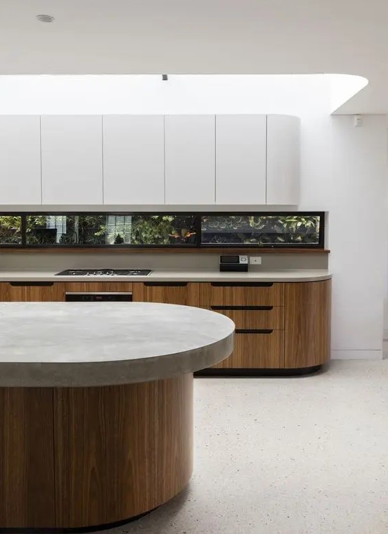 a minimalist kitchen with stained and sleek white curved cabinets, a window backsplash and a curved kitchen island with a stone countertop