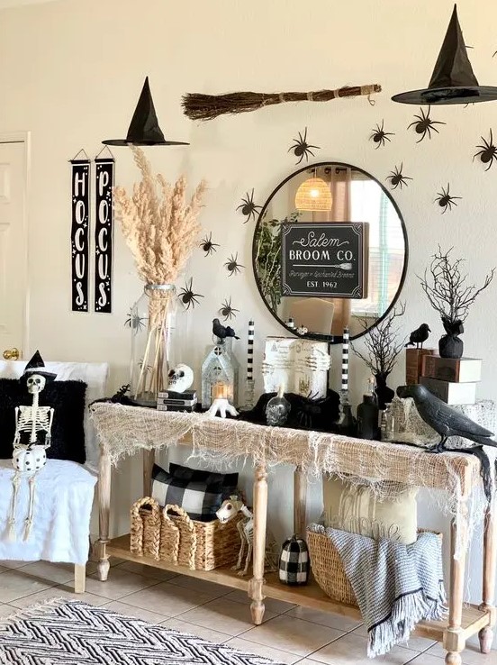 a Halloween console with neutral cheesecloth, blackbirds, spiders, a round mirror, lanterns and candles and pampas grasses