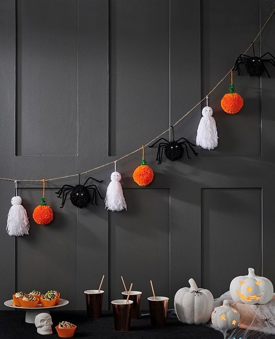 a Halloween garland of white tassels as ghosts, black spiders and orange pumpkin pompoms is a cool idea for styling a kids' party