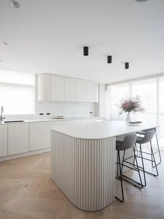a minimalist white kitchen with curved cabinets, a white marble backsplash, a curved ribbed kitchen island and tall grey stools