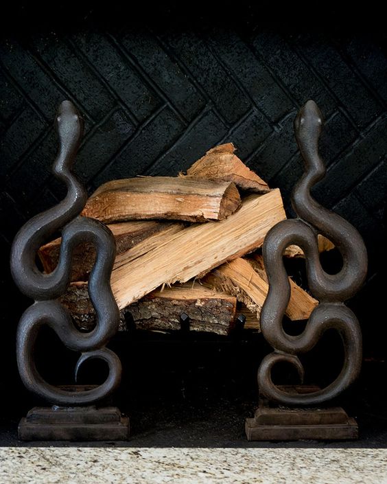 a non-working fireplace with firewood accented with two black snake stands is a creative and scary idea