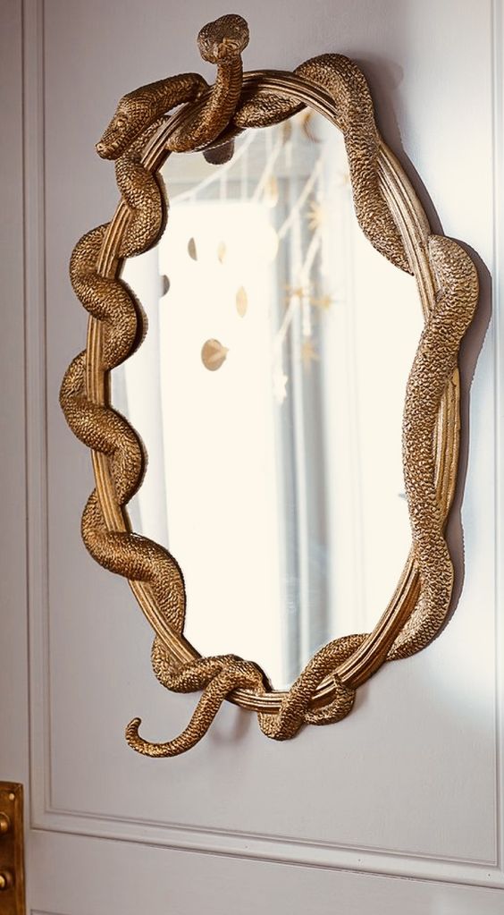 a mirror in a gilded frame with gold snakes is a chic and refined decor idea for Halloween
