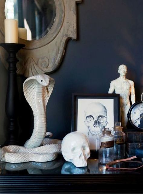 Halloween console table styling with a black cobra snake, a skull, a skull print and some poison bottles