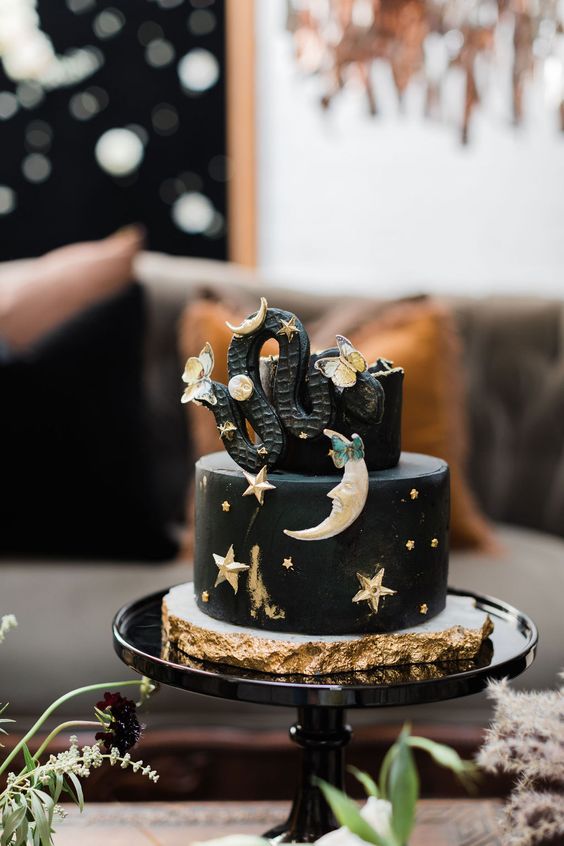 a black celestial Halloween cake with gold stars and moons, a black snake and butterflies is great for the party