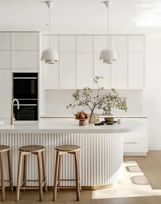 a sophisticated contemporary kitchen in white, with a white stone backsplash and countertops, a curved fluted kitchen island, pendant lamps
