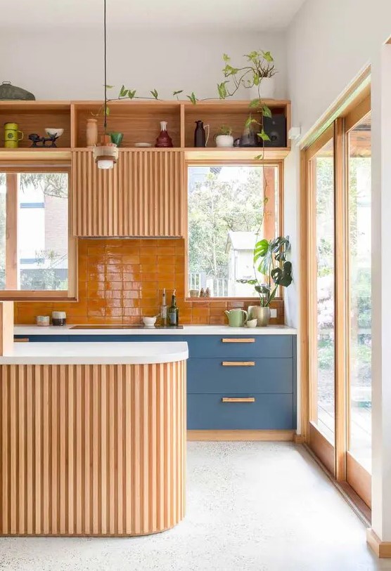 a welcoming warm-colored kitchen with blue cabinets, an orange backsplash and some light-stained cabinets, a curved kitchen island
