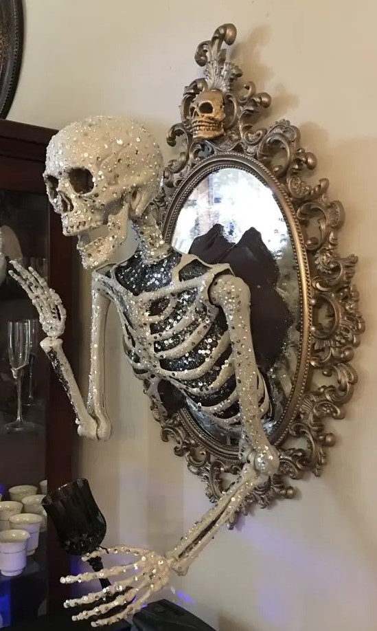 a scary glam Halloween decoration of a vintage mirror with a glam embellished half skeleton attached is elegant