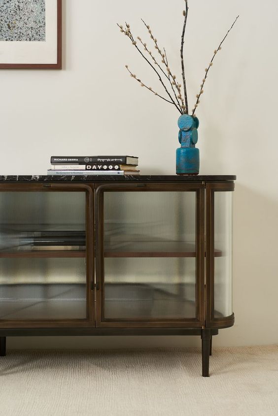 a curved credenza with reeded glass and dark framing, tall black legs and a black stone countertop is an elegant idea for a mid-century modern space