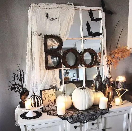 vintage Halloween decor in black and white, with a vintage mirror, some spiderweb, white pumpkins and candles, leaves and branches