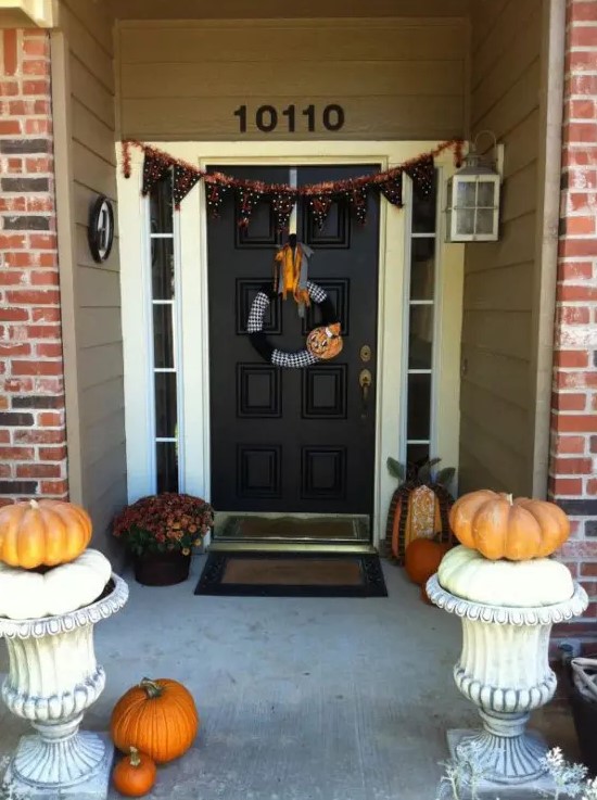 a simple Halloween porch styled with blooms and pumpkins plus a black and orange printed bunting is a very easy idea