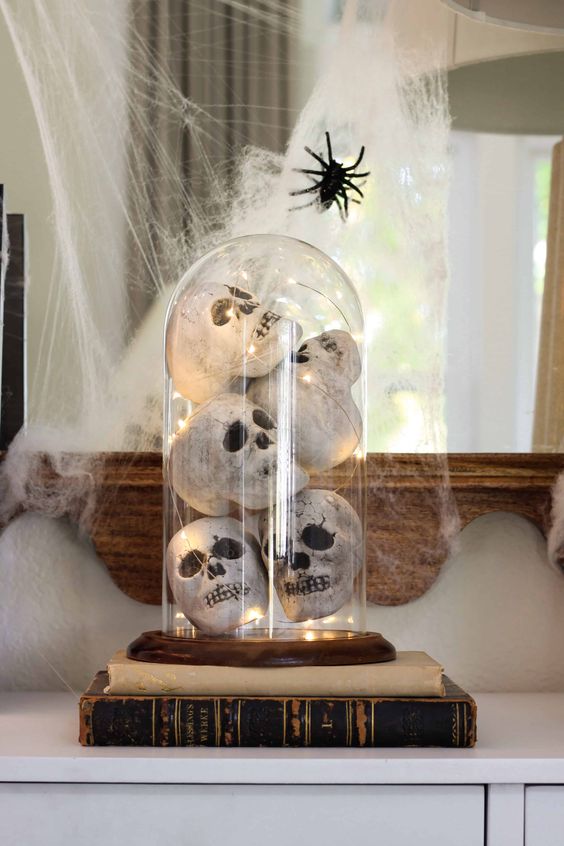 Halloween decor with books, a cloche with faux skulls and lights and spiderweb and a spider is easy to make