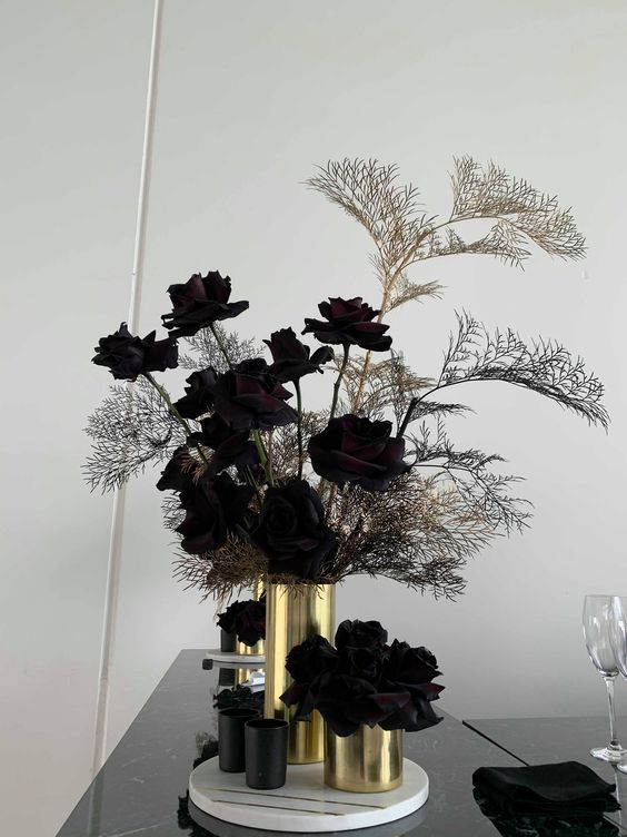 a Halloween arrangement of very dark, almost black roses and some branches in black and gold vases