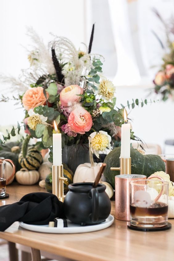 a Halloween centerpiece of coral and white and yellow blooms, greenery, twigs and feathers is a cool arrangement