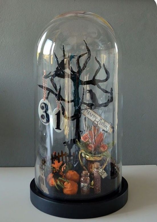a Halloween cloche with a black tree with numbers, some pumpkins and bright blooms in a planter is a cool Halloween scene