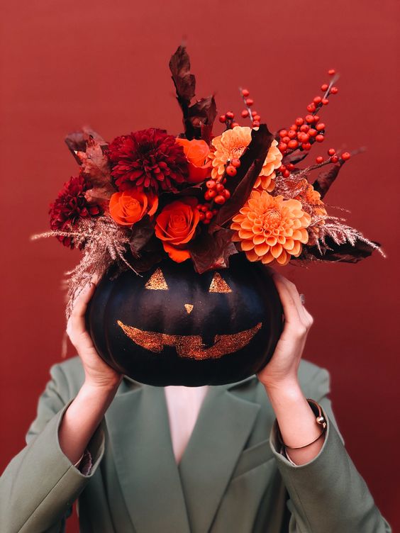 a Halloween decoration of a black painted pumpkin with burgundy and orange blooms, berries, dark foliage and herbs
