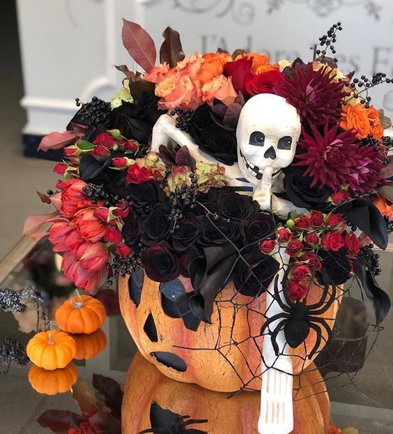 a Halloween decoration of a pumpkin, a spiderweb and a spider, bold red, orange and burgundy blooms, deep red callas and a skeleton